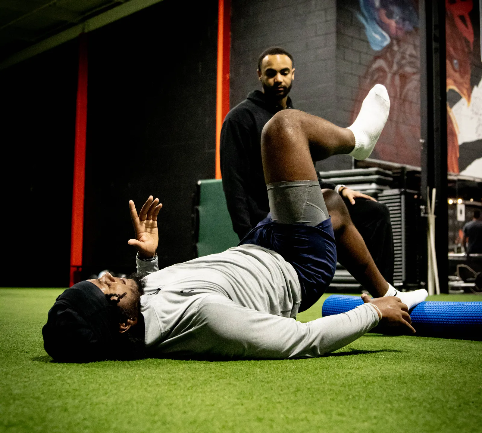 A HAUS coach watching an athlete work through a hip mobility drill on turf