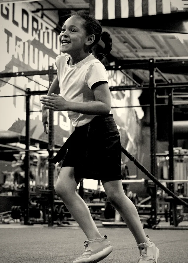 A young HAUS athlete sprinting against a resistance band on turf, smiling mid-stride